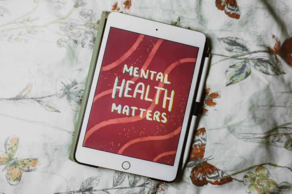 An iPad with the text "Mental Health Matters" displayed on the screen, resting on a bed with floral bedding.