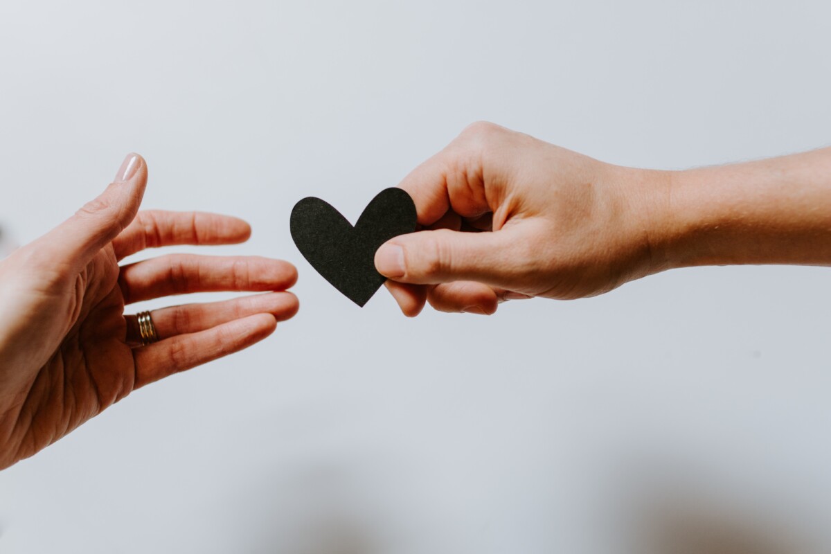 Two hands reaching towards each other, one hand passing a black heart to the other, symbolizing support and care in mental health.